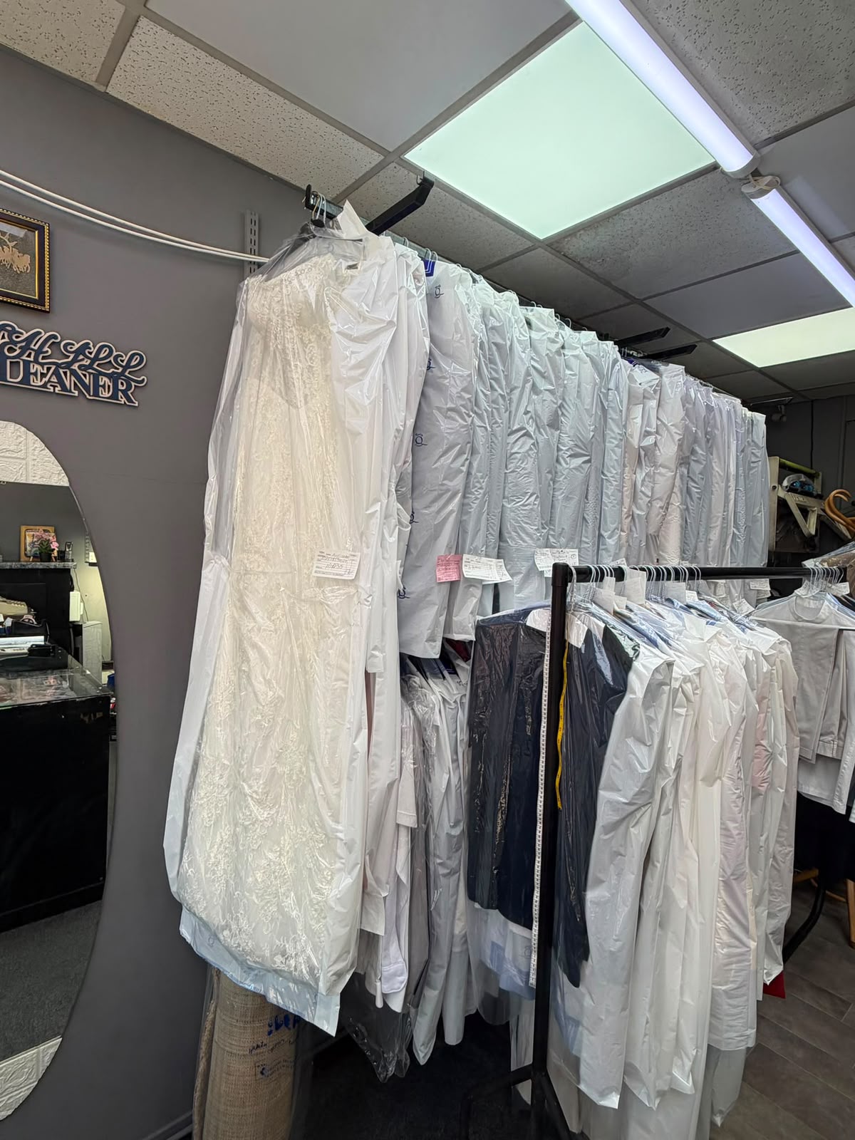 Garments and a wedding dress hanging inside Gants Hill Dry Cleaners